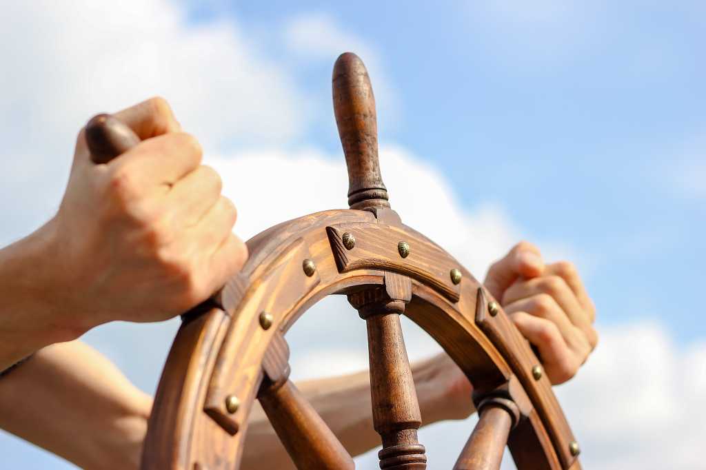 Steering hand wheel ship on sky background, hand hold hand wheel