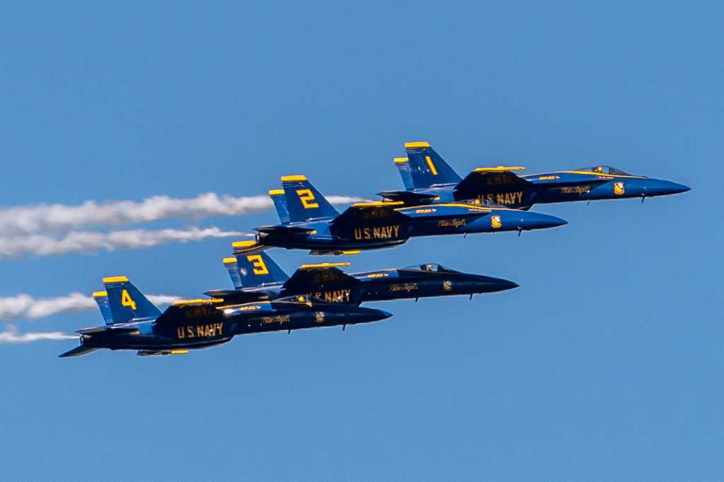 Four US Navy Blue Angels fighter jets numbered 1 2 3 4 flying in formation during San Francisco Fleet Week 2023. Blue jets with gold trim against a clear blue sky
